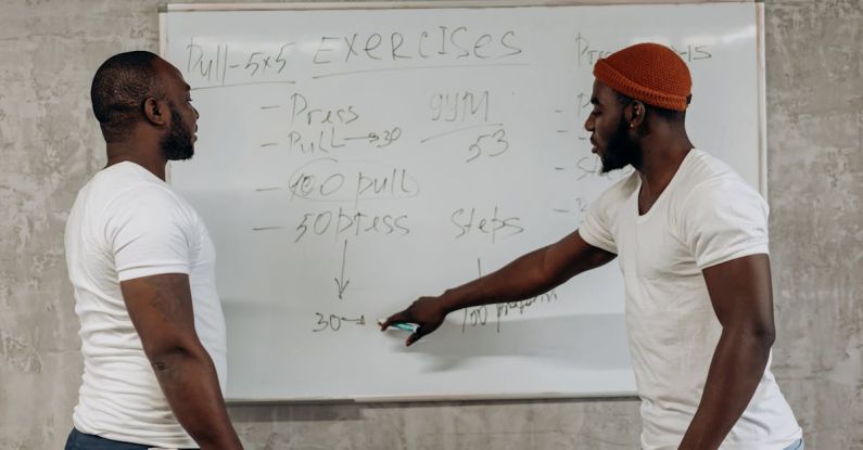 Training Schedule - Two Men Looking At A Workout Schedule On A Whiteboard