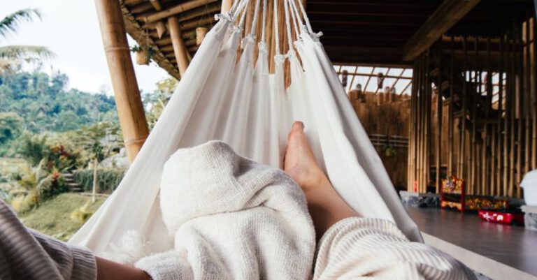 Rest Days - Crop barefoot traveler chilling on white cozy hammock under blanket on terrace of house in daytime