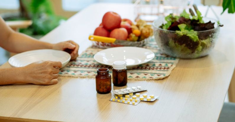 Recovery Foods - From above of crop anonymous person sitting at table with pile of various medicines and bowls of fresh lettuce salad and ripe fruits in kitchen