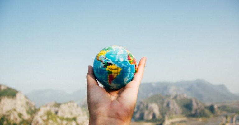 Traveling - Person Holding World Globe Facing Mountain