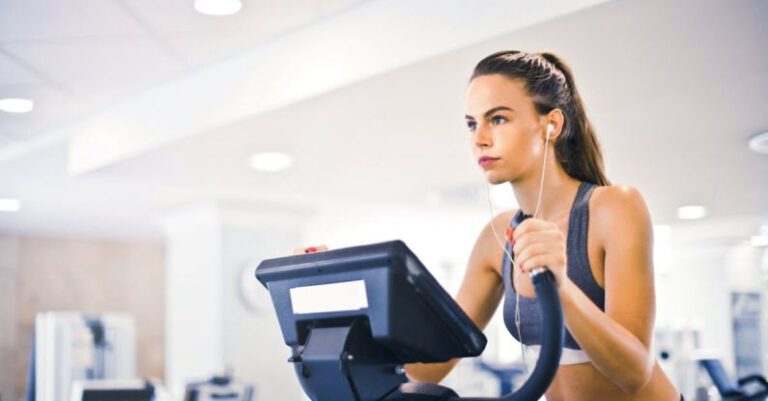 Cardio And Strength - Serious fit woman in earphones and activewear listening to music and running on treadmill in light contemporary sports center