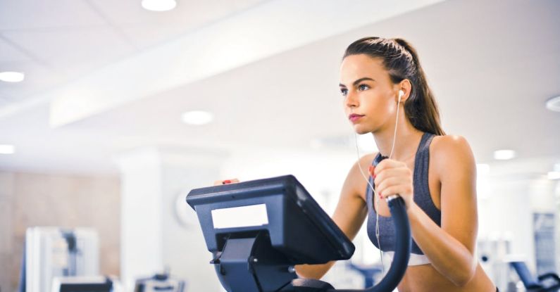 Cardio And Strength - Serious fit woman in earphones and activewear listening to music and running on treadmill in light contemporary sports center